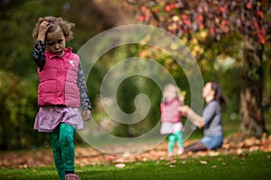 Mother and identical twins having fun under tree with autumn leaves in the park, blond cute curly girls, happy family