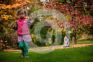 Mother and identical twins having fun under tree with autumn leaves in the park, blond cute curly girls, happy family