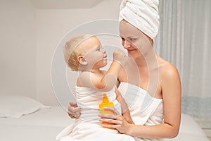 Mother and infant baby boy in white towels after bathing apply sunscreen or after sun lotion. Children skin care in a hotel or