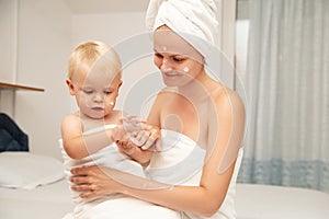 Mother and infant baby in white towels after bathing apply sunscreen or after sun lotion or cream. Children skin care