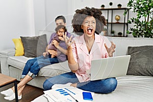 Mother of interracial family working using computer laptop at home crazy and mad shouting and yelling with aggressive expression