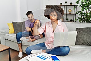 Mother of interracial family working using computer laptop at home pointing down looking sad and upset, indicating direction with