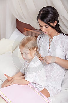 Mother and kid daughter read a book together in bed