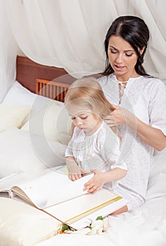 Mother and kid daughter read a book together in bed