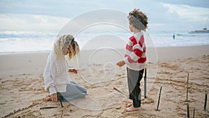 Mother kid resting ocean shore on windy day. Beautiful family drawing beach sand