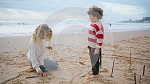 Mother kid resting ocean shore on windy day. Beautiful family drawing beach sand