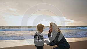 Mother kid resting shore on autumn sunset together. Smiling woman talking phone