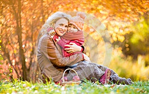 Mother and kid sitting and hugging together in autumn park.