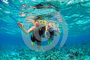 Mother, kid in snorkeling mask dive underwater with tropical fishes