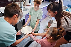 Mother with kids cooking at kitchen, happy children`s moments. Cheesecake in the oven