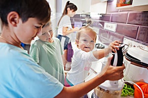 Mother with kids cooking at kitchen, happy children`s moments. Work with a blender