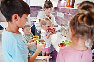 Mother with kids drink compote at kitchen, happy children`s moments