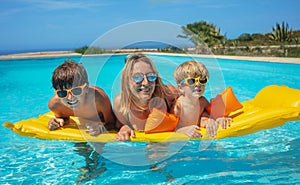 Mother with kids enjoying pool time float on yellow mattress
