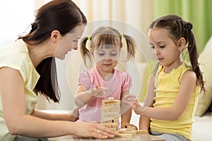 Mother with kids play board game in living room. Family spending time together at home