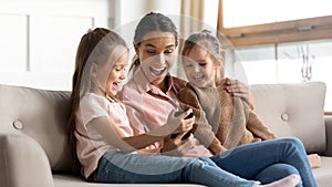 Mother and kids sit on couch having fun using smartphone