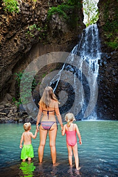 Mother with kids swim in water pool under waterfall