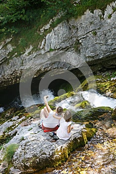 Mother with kids taking a selfie, sitting on a rock by a mountain stream on a family trip