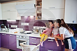 Mother kiss her girls kids at kitchen, happy children`s moments. Mom and two daughters
