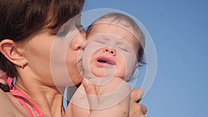 Mother kisses baby against blue sky.