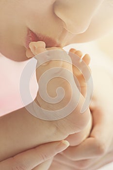 Mother kisses baby feet, closeup. Daylight. Selective focus.