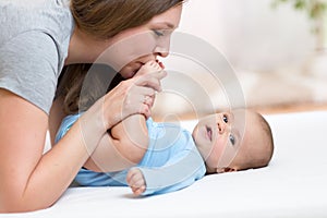 Mother kisses baby feet while play on a white bed