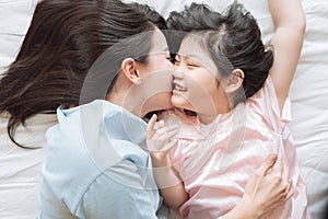 Mother kisses her daughter cheek. and hugging in the bedroom .Happy Asian family.