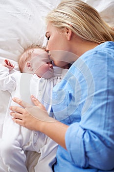 Mother Kissing Baby Girl As They Lie In Bed Together