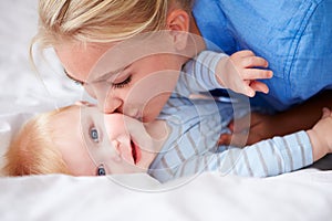 Mother Kissing Baby Son As They Lie In Bed Together