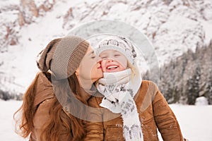 Mother kissing child outdoors among snow-capped mountains