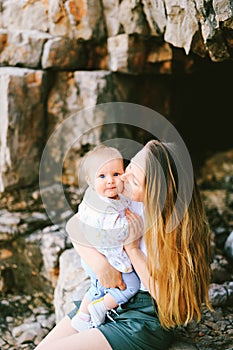 Mother kissing her baby on the cheek while sitting on a rocky beach in Montenegro