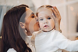 Mother kissing her daughter in cheek. room decorated for Christmas.