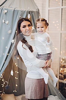 Mother kissing her daughter in cheek. room decorated for Christmas.