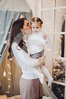 Mother kissing her daughter in cheek. room decorated for Christmas.