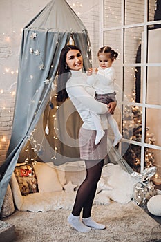 Mother kissing her daughter in cheek. room decorated for Christmas.