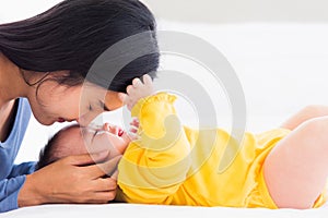 Mother kissing her infant newborn baby in a white bed