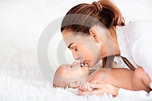 Mother kissing her newborn baby laying on soft white background. Copy space