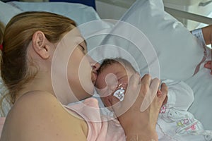 A mother kissing her newborn baby sleep in bed