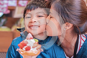 Mother kissing her son smiling while eating strawberry dessert ice cream in japanese cafe