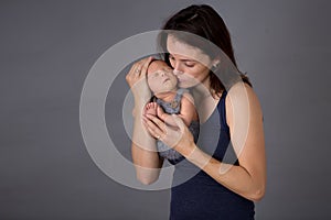 Mother kissing and hugging newborn son at gray background, tender, care, love