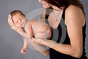 Mother kissing and hugging newborn son at gray background, tender, care, love