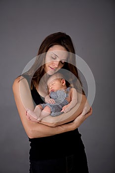 Mother kissing and hugging newborn son at gray background, tender, care, love