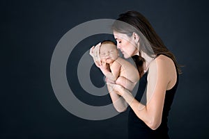 Mother kissing and hugging newborn son at gray background, tender, care, love