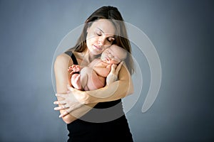 Mother kissing and hugging newborn son at gray background, tender, care, love