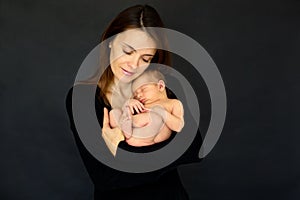 Mother kissing and hugging newborn son at gray background, tender, care, love