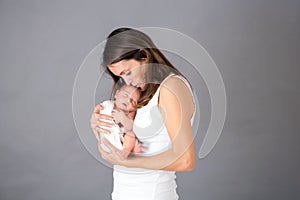 Mother kissing and hugging newborn son at gray background, tender, care, love