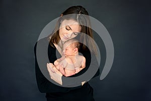 Mother kissing and hugging newborn son at gray background, tender, care, love