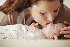 Mother Kissing Newborn Baby Lying On Changing Table In Nursery