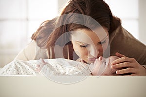 Mother Kissing Newborn Baby Lying On Changing Table In Nursery