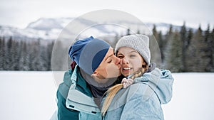 Mother kissing small daughter outdoors in winter nature, Tatra mountains Slovakia.