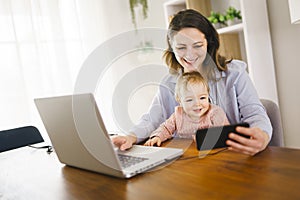 mother in kitchen home office with computer and laptop at home with her daugher